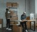 Two workers handling packages and organizing stock in a warehouse setting.